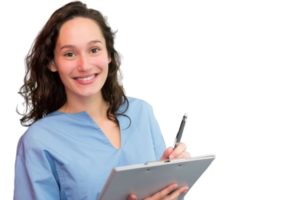 woman in scrubs smiling and writing on clipboard